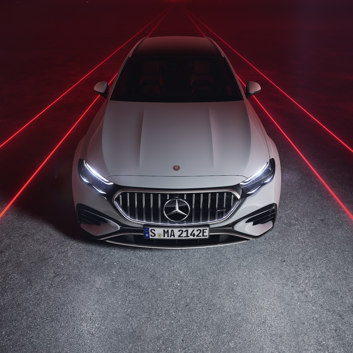 Mercedes-AMG E 53 HYBRID 4MATIC+ 在紅色背景下從上方視角看的車頭視圖。