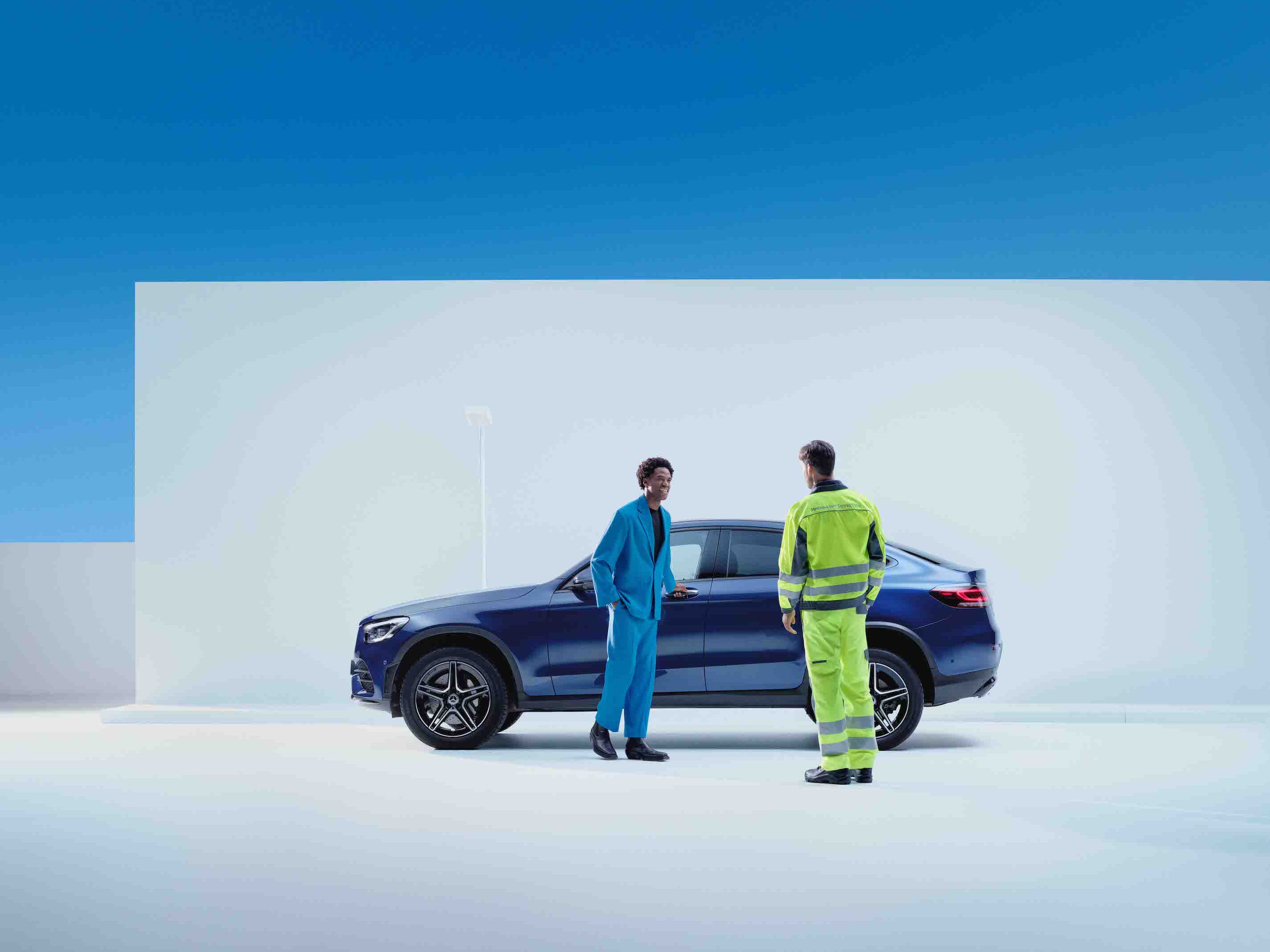 一名男子和一名服務員工站在一輛 Mercedes-Benz 車前。