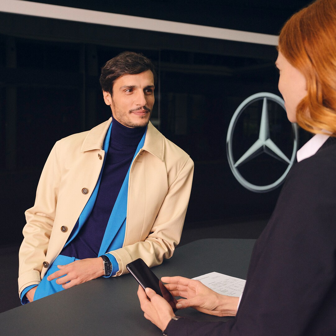 一位顧客倚靠著櫃檯，滿懷期待地轉向 Mercedes-Benz 員工。